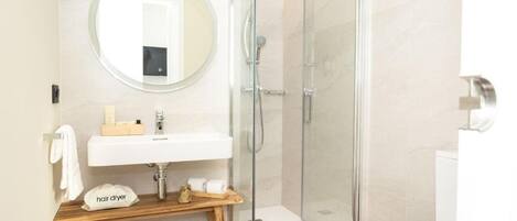 A modern bathroom with a glass-enclosed shower, a round mirror, a wooden vanity, and a toilet with a gold accent.