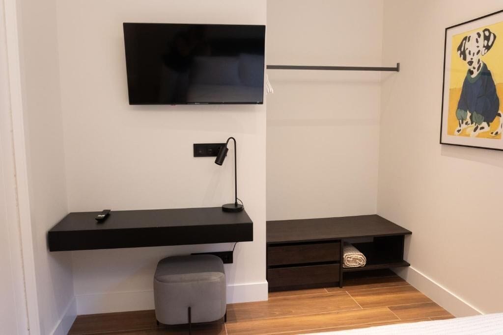 A modern room with a flat-screen TV mounted on the wall, a desk with a lamp, and a framed picture of a Dalmatian.