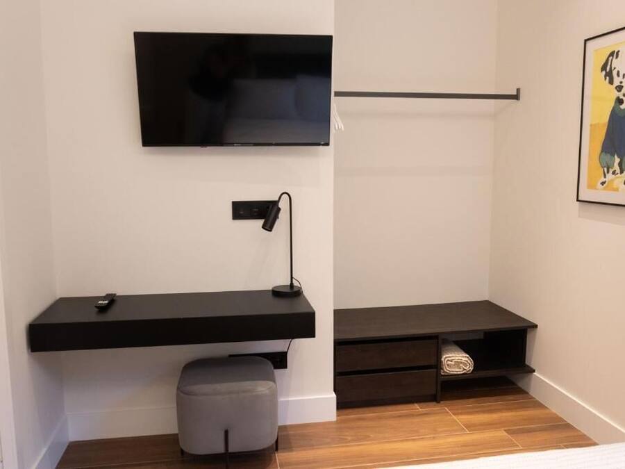 A modern room with a flat-screen TV mounted on the wall, a desk with a lamp, and a framed picture of a Dalmatian.