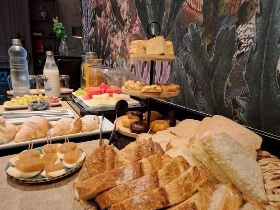 Una mesa de buffet con diferentes opciones de comida, incluyendo pan, bollería y fruta.