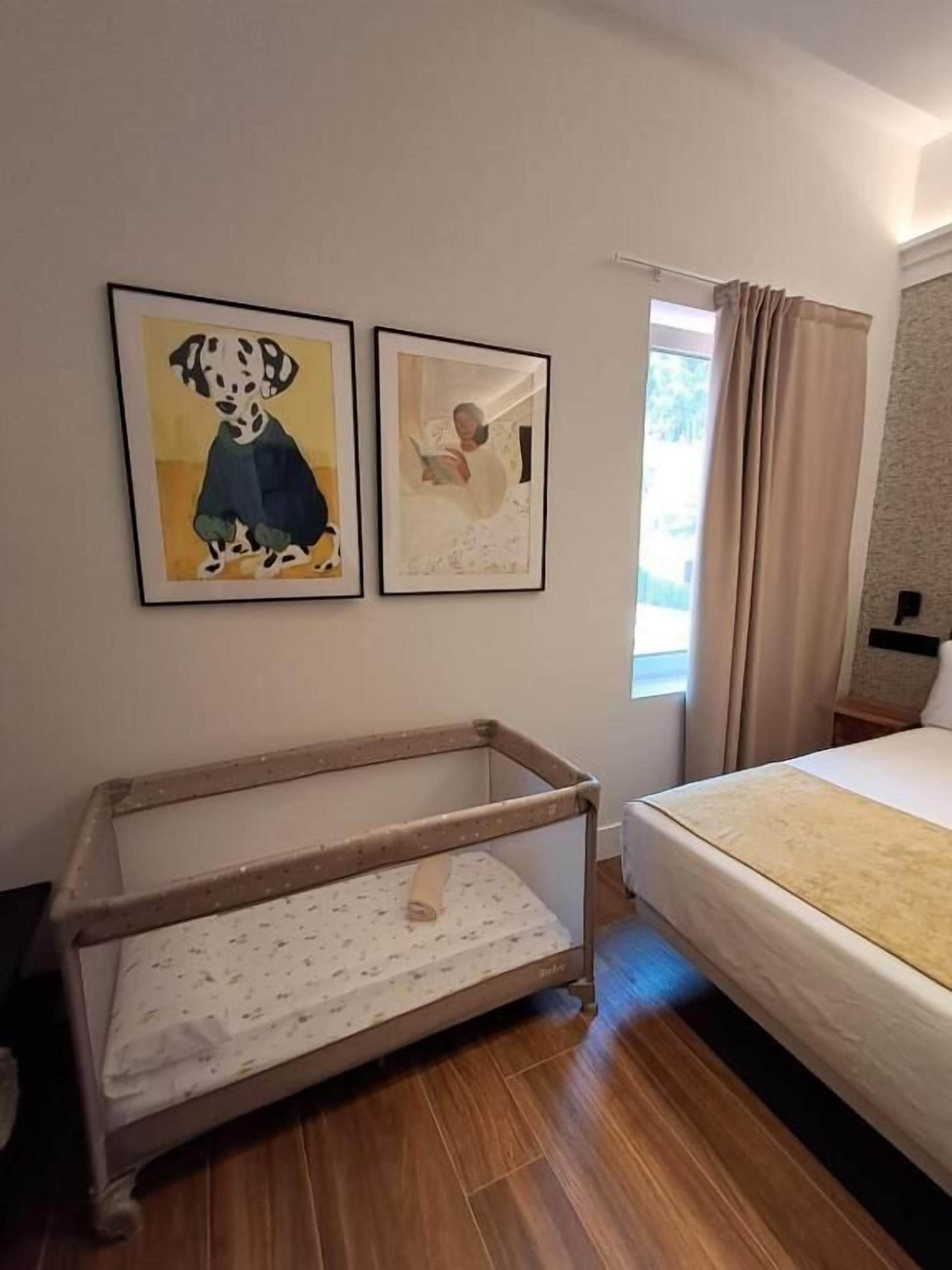 Een kamer met een bed, een babybedje en twee foto's in lijsten aan de muur.