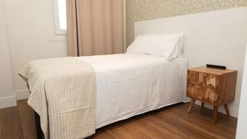 Un dormitorio con una cama, una mesita de noche de madera, una ventana con cortinas y un muro con textura.