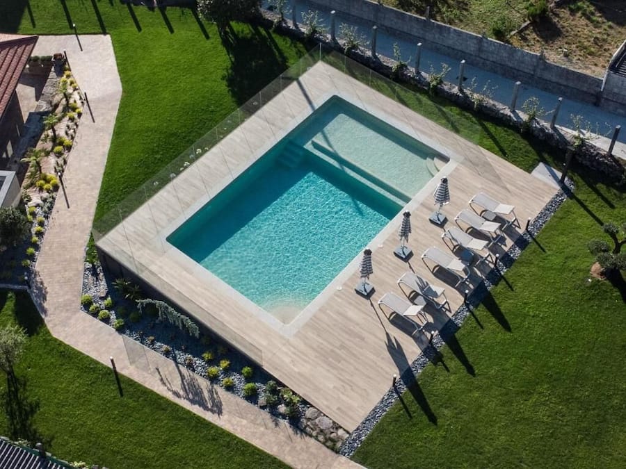 En vy från ovan av en rektangulär swimmingpool med en kakelbeklädd poolkant, omgiven av en välskött gräsmatta och en mur av sten.