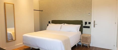 Una habitación de hotel ordenada con una cama grande, una mesita de noche, un espejo y una puerta.