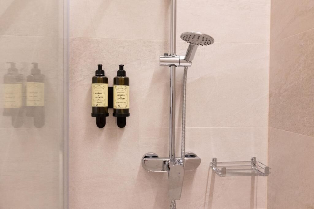 A shower with a handheld showerhead and a wall-mounted bottle of shampoo and conditioner.