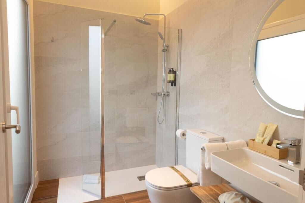 A modern bathroom with a glass-enclosed shower, a toilet, and a sink with a mirror.