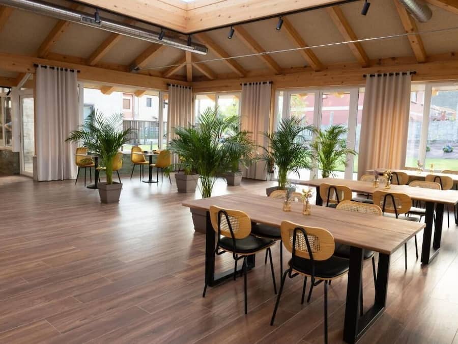 Un espacio interior amplio con suelo de madera, varias mesas y sillas, y plantas en macetas.