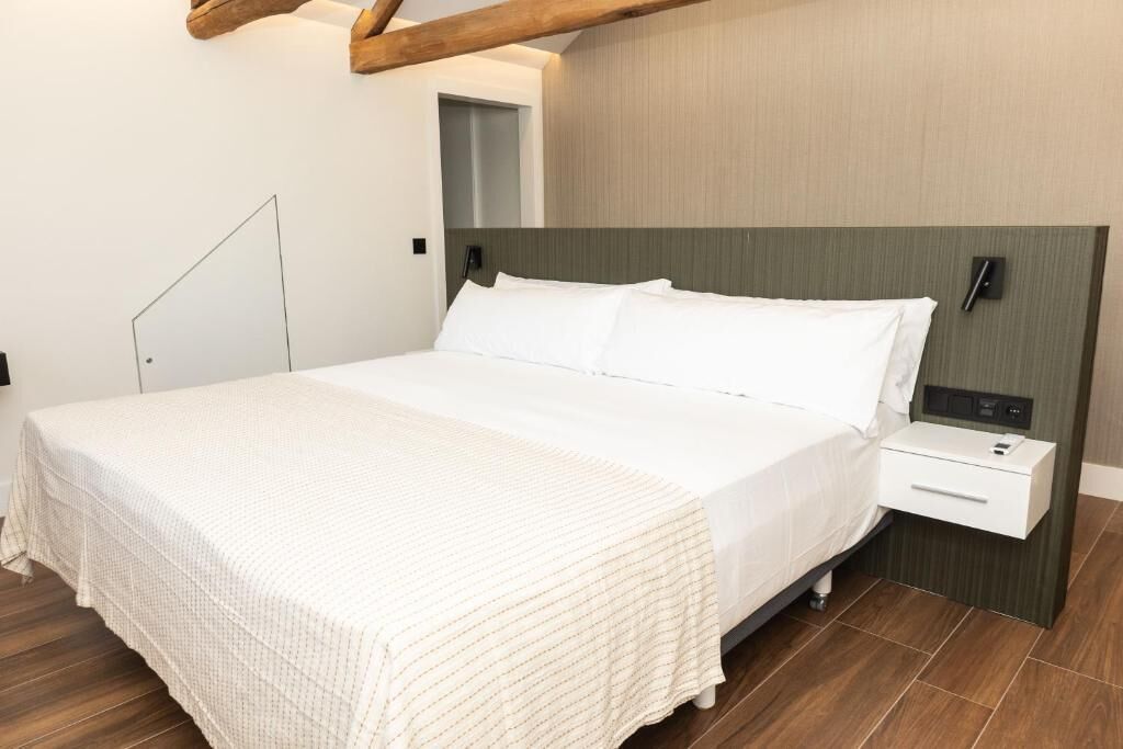 Una habitación de hotel moderna con una cama grande, una mesita de noche y una viga de techo de madera.