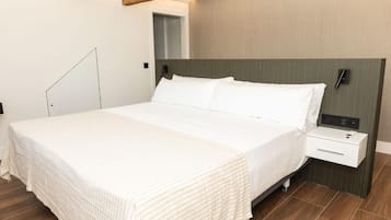 A modern hotel room with a large bed, a bedside table, and a wooden ceiling beam.