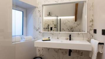 Une salle de bain moderne avec un grand miroir, un lavabo blanc et un papier peint à motifs floraux.