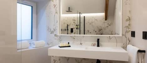 Un baño moderno con un espejo grande, lavamanos blanco y papel tapiz floral.