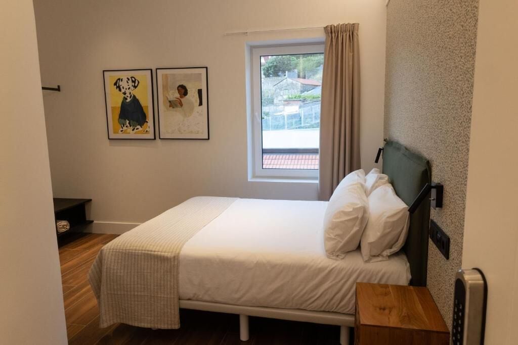 Un dormitorio con una cama, una ventana con cortinas y dos cuadros en la pared.