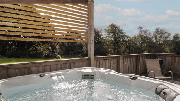 A hot tub with a wooden deck and a pergola overhead. - The Lodge (Bridgend)