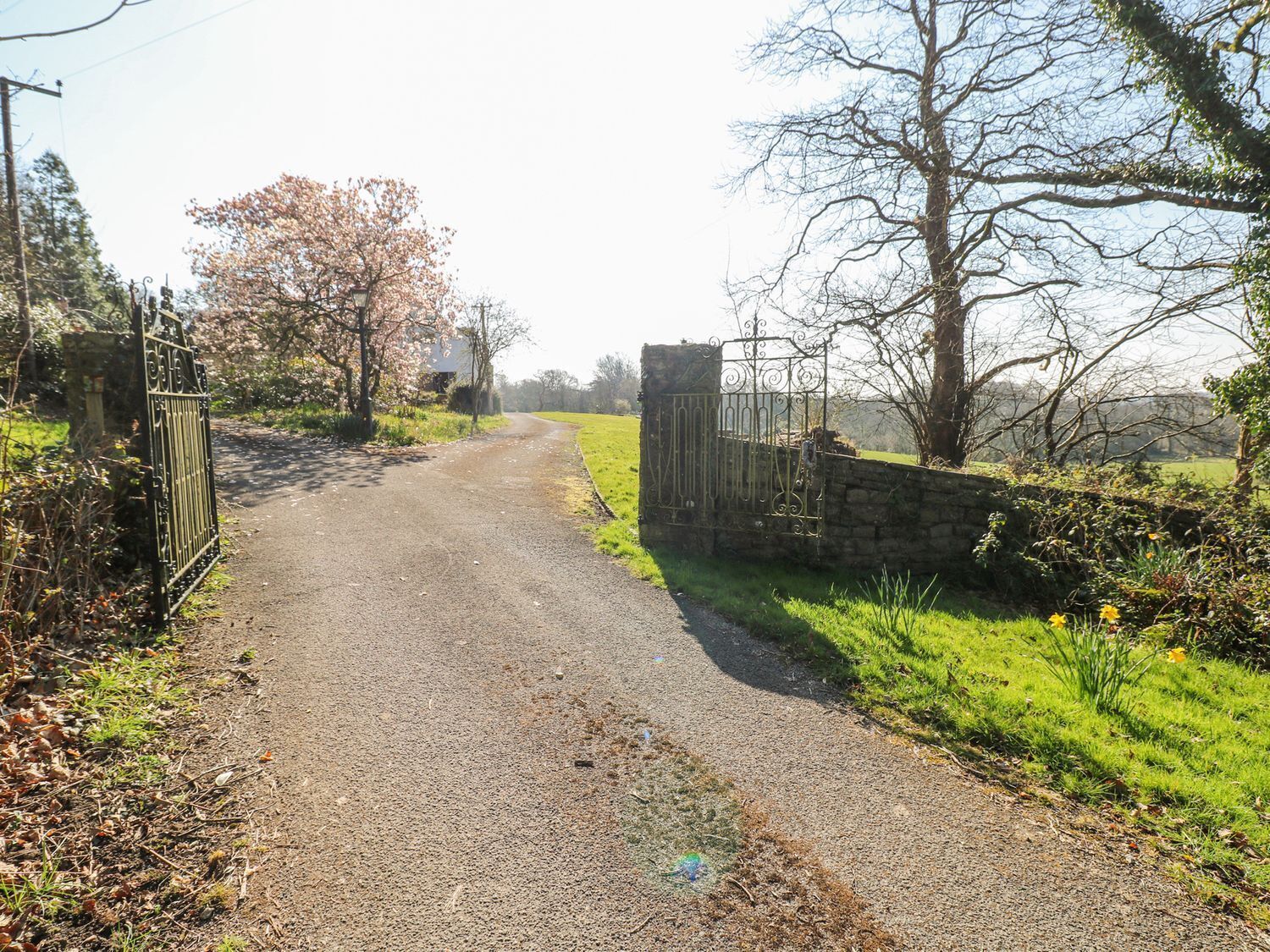 A rural road leading to a gated property with a stone wall and metal gate.