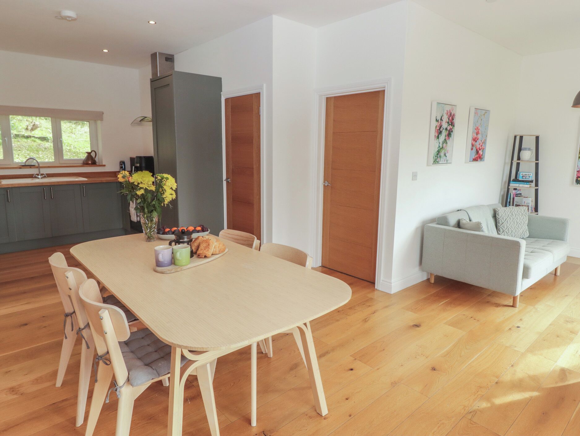 Una cocina moderna con armarios grises, una mesa de comedor de madera con sillas, y un sofá gris en una sala de estar.