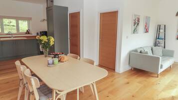 Una cocina moderna con armarios grises, una mesa de comedor de madera con sillas, y un sofá gris en una sala de estar.