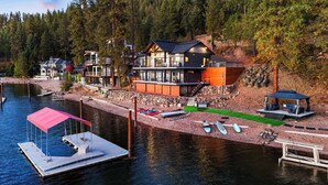 Una cabaña junto al lago con un muelle, kayaks y una zona de estar cubierta.