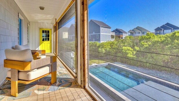 A balcony with a glass-enclosed pool, a wooden chair, and a yellow door. - A Mindful Break | Private Pool | EV Charger | Full Gym (Surf City)