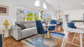 A spacious living room with a grey sofa, blue chairs, a round table, and a white bar area. - A Mindful Break | Private Pool | EV Charger | Full Gym (Surf City)