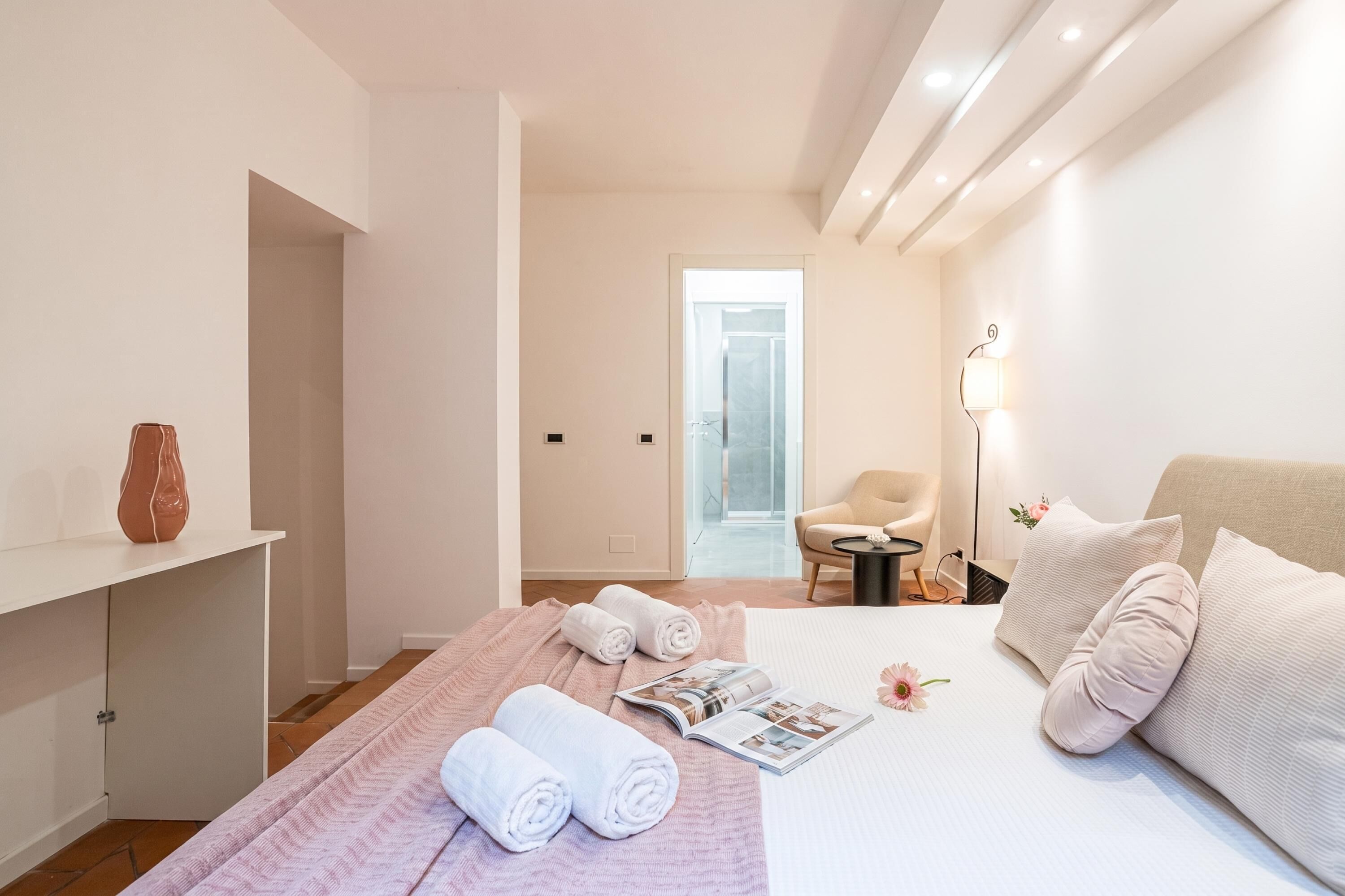A hotel room with a bed, a small table, a chair, and a bathroom visible through an open door.