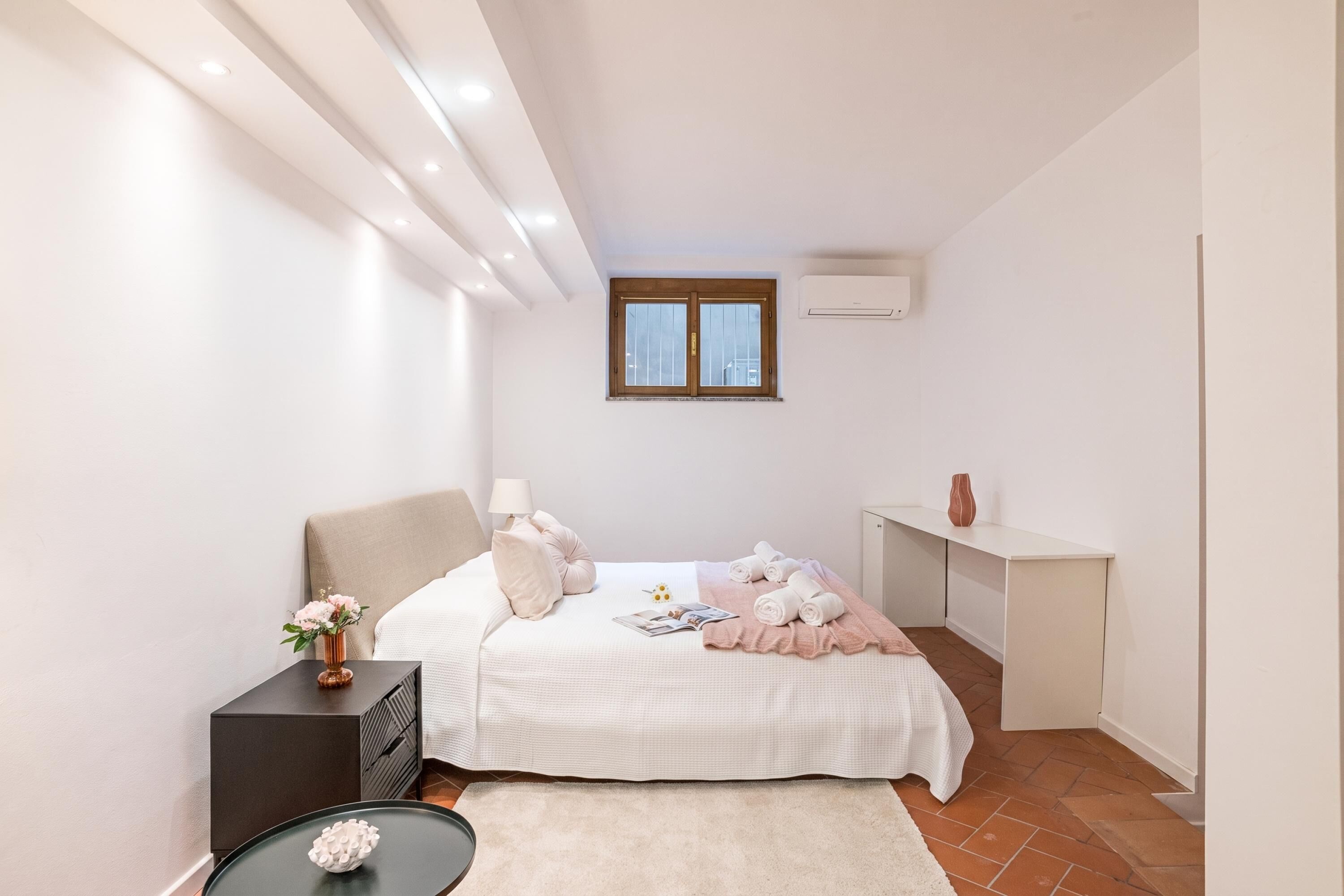 A bedroom with a bed, bedside table, lamp, and a window.