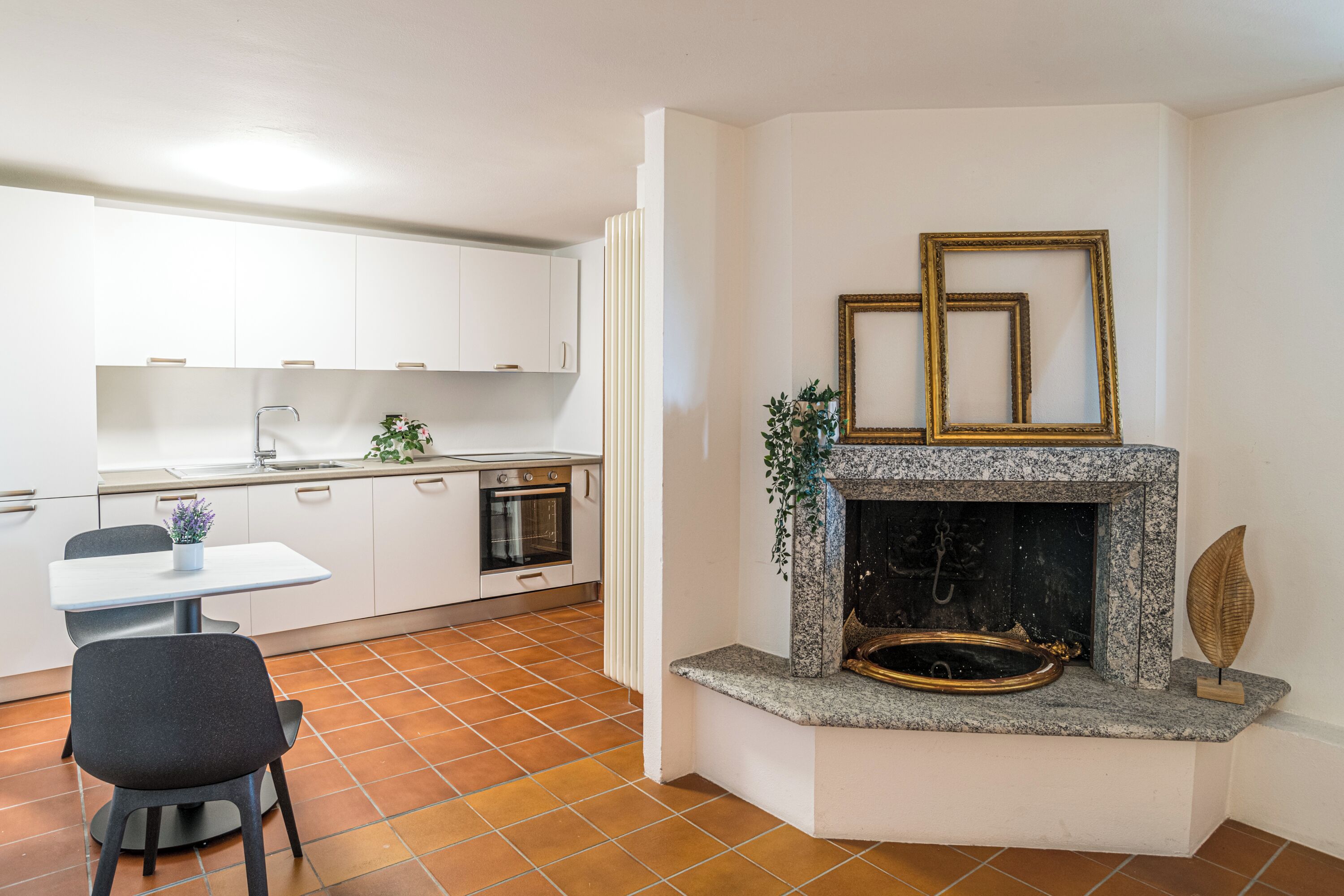 A modern kitchen with white cabinets, a built-in oven, and a fireplace with decorative items.