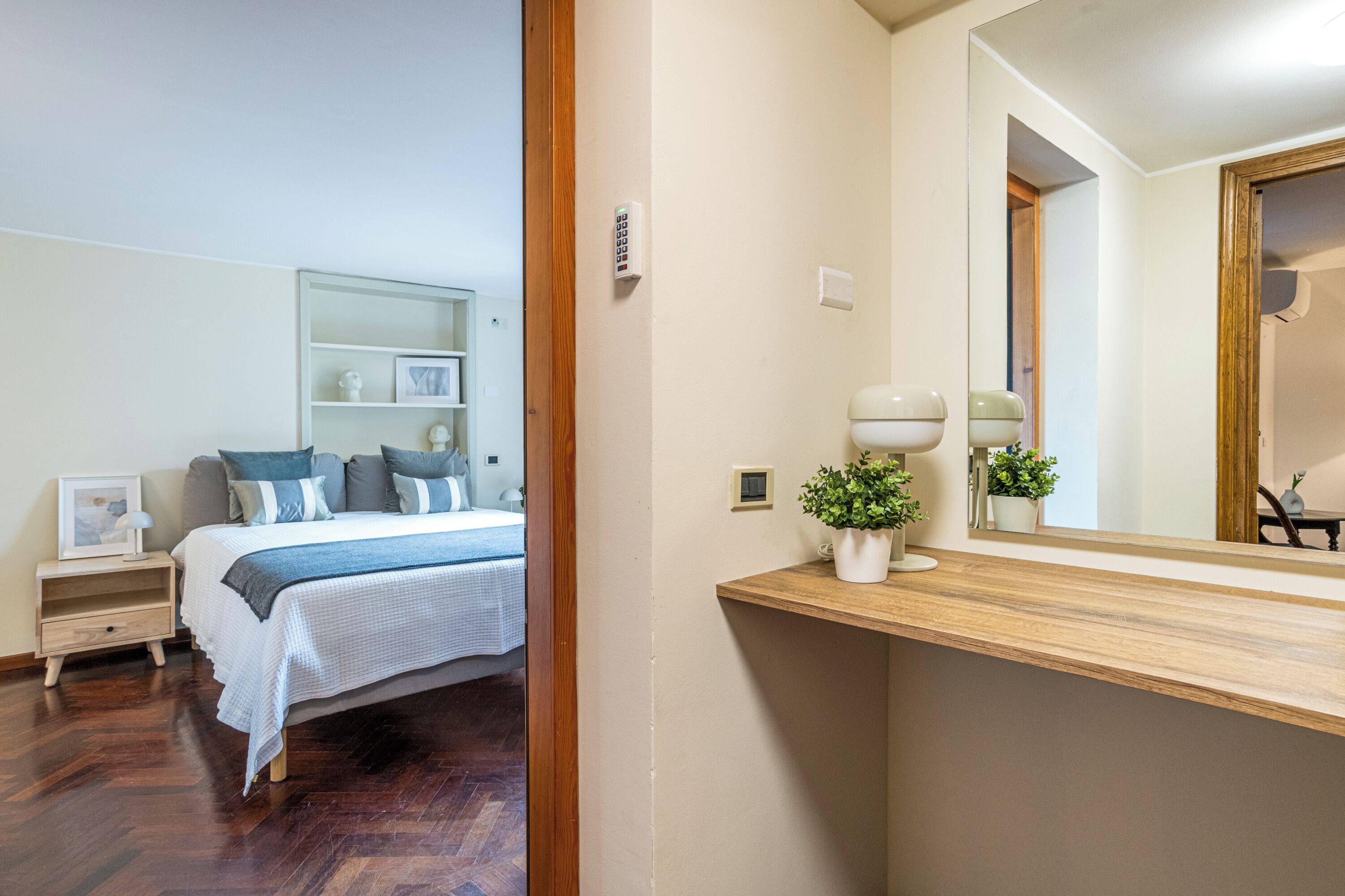 A bedroom with a bed, bedside table, nightstand, and a mirror above the sink.
