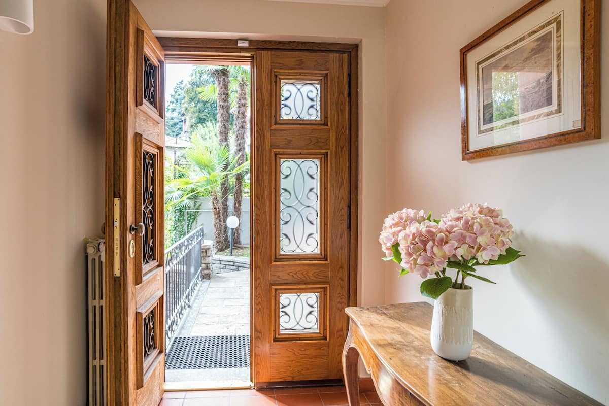 A wooden door with decorative glass panels, a white vase with pink flowers on a wooden table, and a framed picture on the wall.