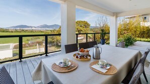 Un coin repas avec une table dressée pour deux personnes, une vue sur le paysage et une montagne à l'horizon.