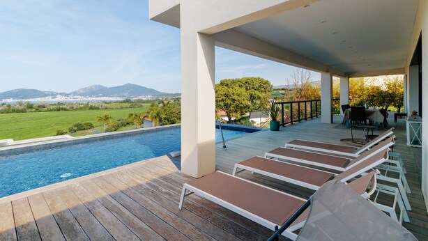 Un espace aménagé au bord de la piscine, avec des chaises longues, une terrasse en bois et une vue sur une chaîne de montagnes.
