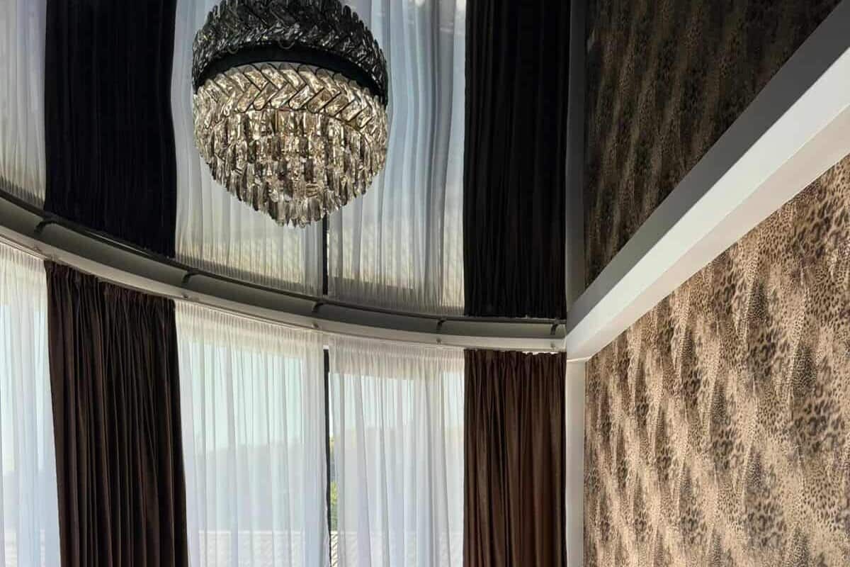 A bedroom with a large bed, a chandelier, sheer curtains, and a patterned wall.