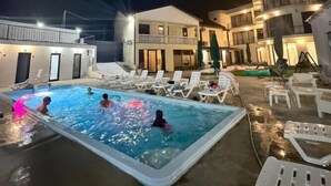Ein Poolbereich bei Nacht mit Liegestühlen und einem Gebäude im Hintergrund.