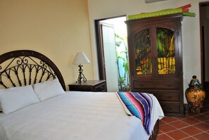 A bed with white linens, a wooden nightstand with a lamp, a wooden cabinet with glass doors, and a colorful woven blanket on the bed. - Stunning home with breathtaking views and steps from Community Pool (Loreto)