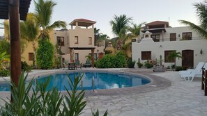 A pool area with lounge chairs, palm trees, and a building with a tiled roof. - Stunning home with breathtaking views and steps from Community Pool (Loreto)