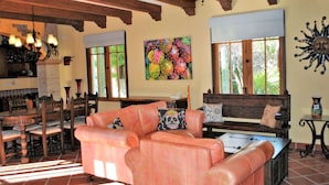 A cozy living room with a fireplace, a dining area with wooden furniture, and a large window with a view of greenery. - Stunning home with breathtaking views and steps from Community Pool (Loreto)