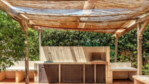 An outdoor kitchen area with a built-in grill, seating, and a pergola providing shade. - Casa Matilde Vista Mare con Piscina by Wonderful Italy (Carrozziere)
