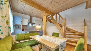 A cozy room with a wooden table, green chairs, a kitchen in the background, and a wooden staircase. - Ferienwohnung Paula (Bad Mitterndorf)