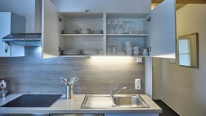 A modern kitchen with a built-in stove, stainless steel sink, and open shelving with dishes and glassware. - Ferienwohnung Paula (Bad Mitterndorf)