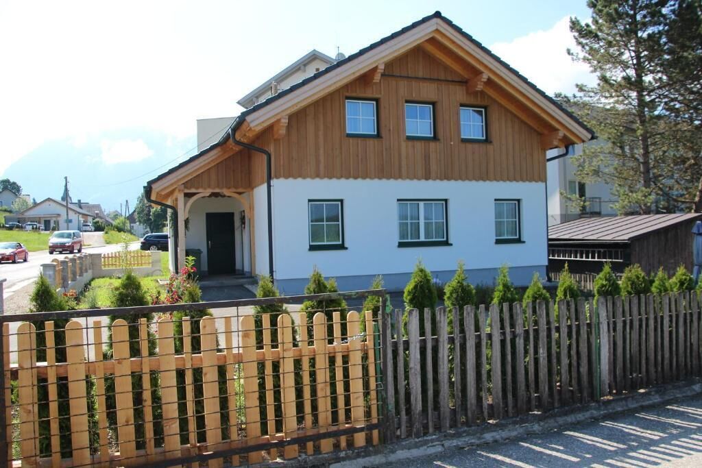 Une maison en bois à deux étages, avec une façade blanche, un porche et une cour clôturée.