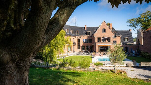 Un grand bâtiment en briques doté d’une piscine, entouré d’une pelouse bien entretenue et d’arbres.