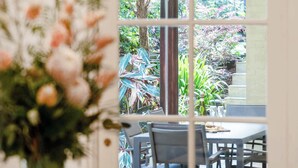 A dining area with a table set for two, a vase of flowers, and a view of an outdoor garden through a glass door. - The Newtown Haven with Private Parking (Newtown)