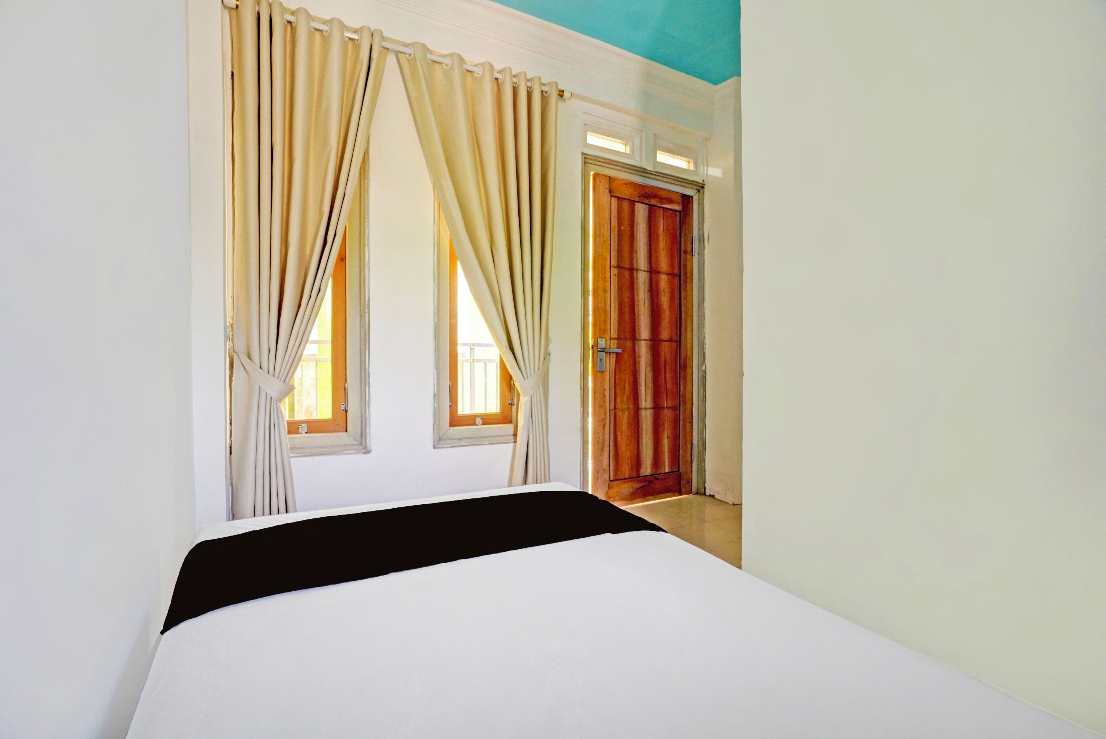 Une chambre à coucher avec un lit, deux fenêtres avec des rideaux, une porte en bois et un plafond bleu.