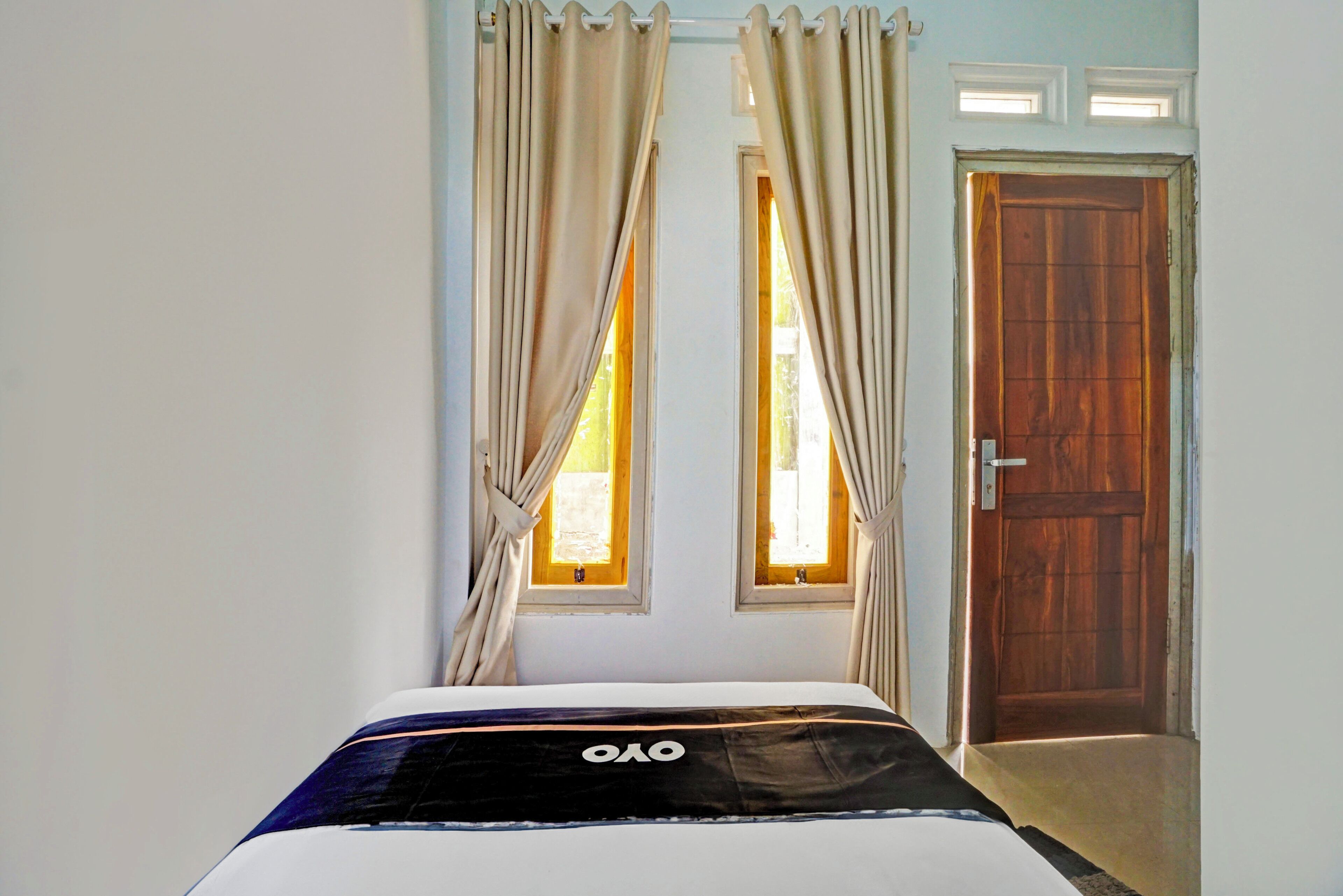 A bedroom with a bed, curtains, a wooden door, and two windows.