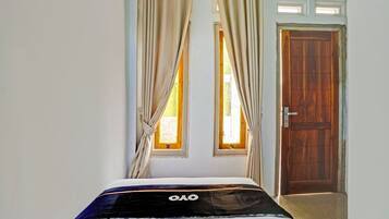 A bedroom with a bed, curtains, a wooden door, and two windows.