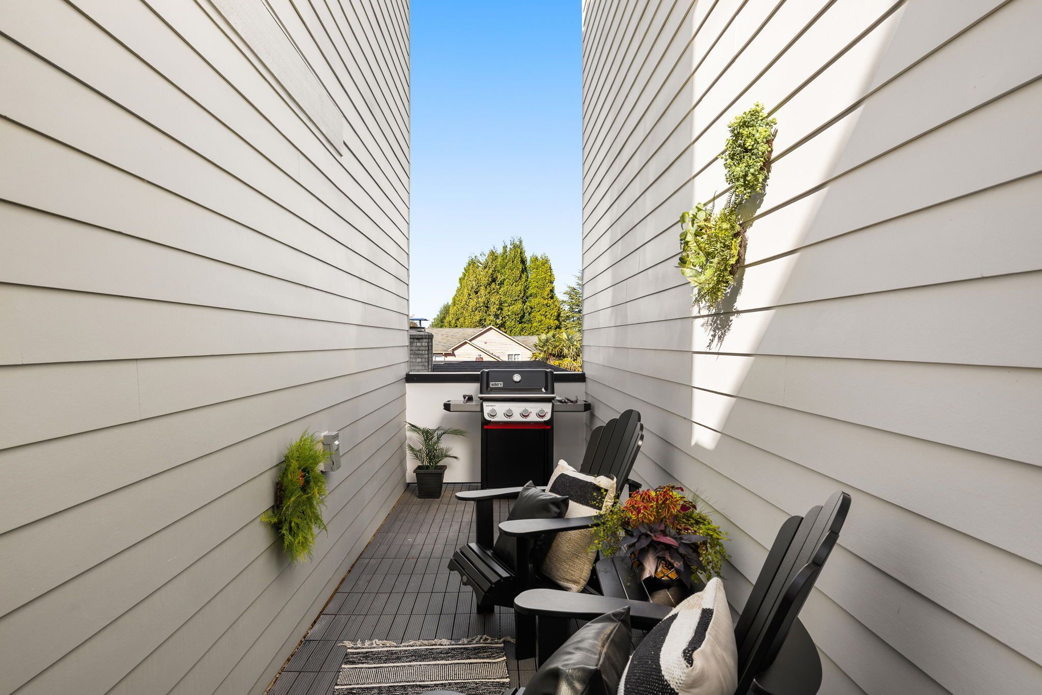 Un pequeño patio exterior con una parrilla, asientos y plantas en macetas.