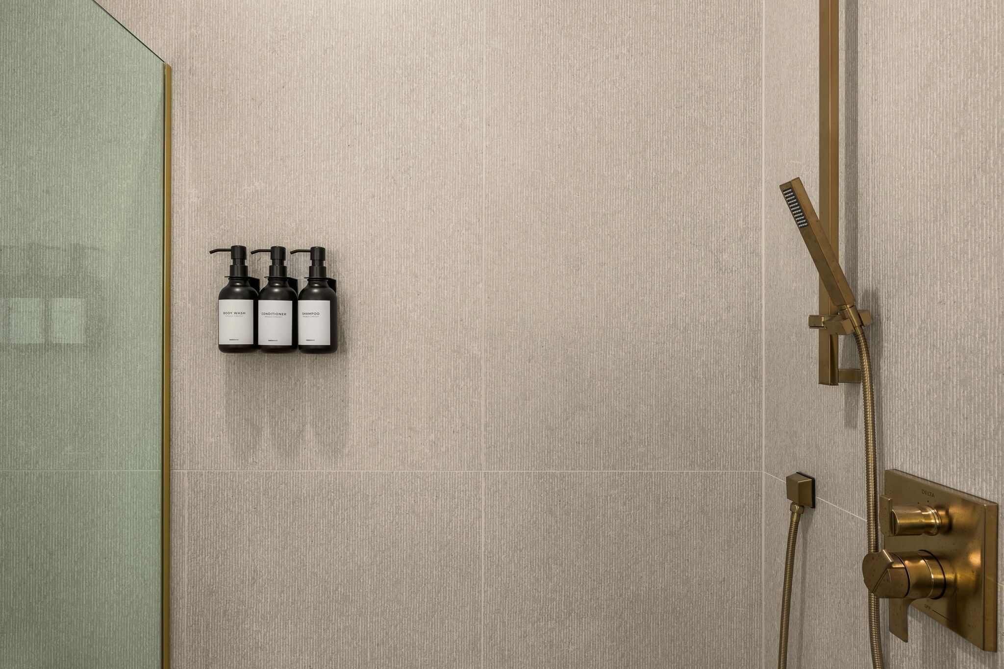 Kylpyhuoneessa on suihku, lasiseinä sekä kolme pulloa shampoota ja hoitoainetta seinällä.
