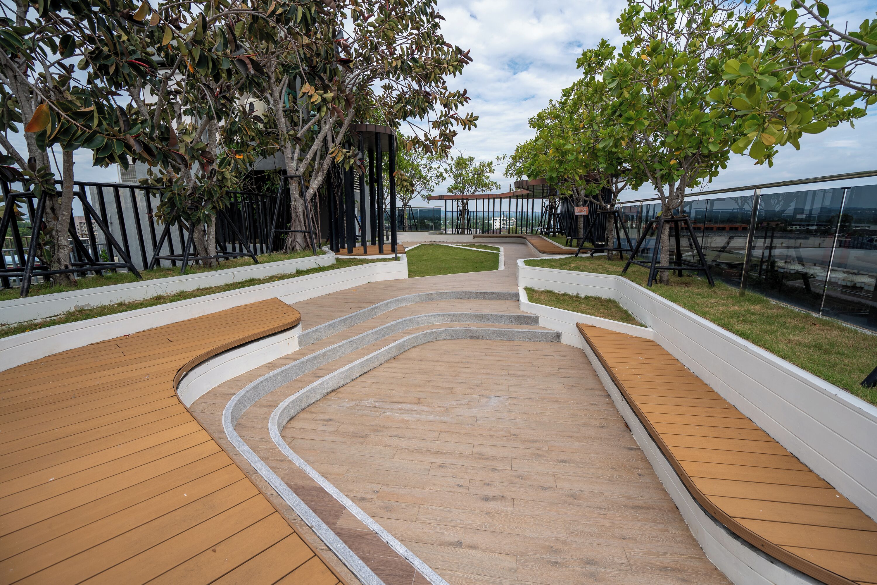 Un'area esterna moderna con passerelle in legno, zone relax e alberi.