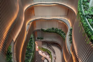 A multi-level atrium with curved wooden railings, a central staircase, and green plants. - Bluphere residence by Prop Hopper (Sattahip)