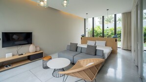 A modern living room with a sofa, a TV, a coffee table, and a wicker chair. - Oceanphere Villa by Prop Hopper (Sattahip)