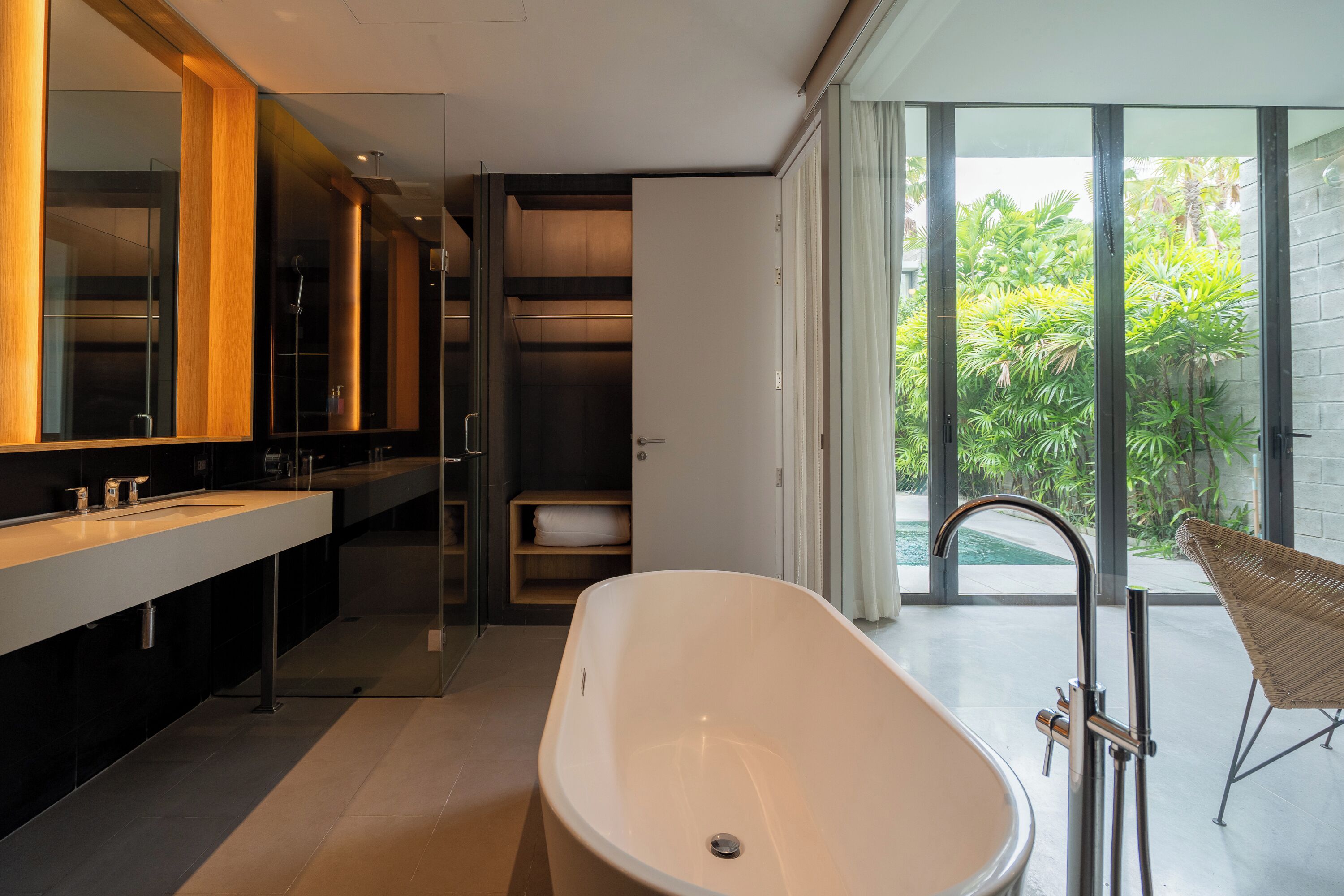 Une salle de bain moderne avec une baignoire sur pieds, un grand miroir et une vue sur la verdure environnante.